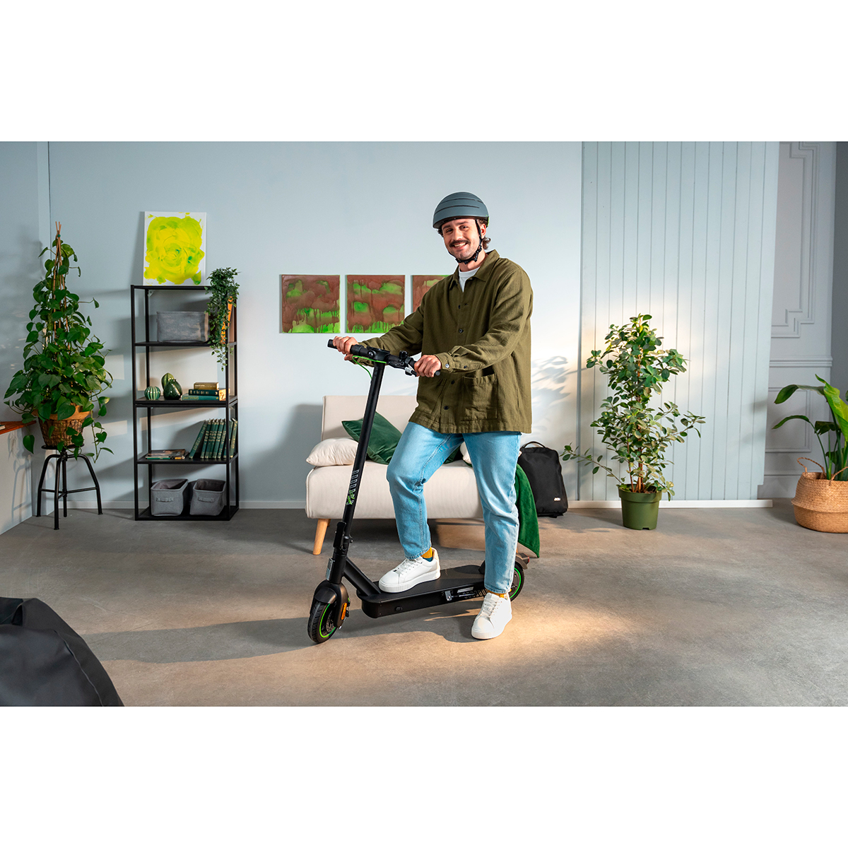 Un hombre con casco está de pie en un patinete eléctrico en un salón moderno.