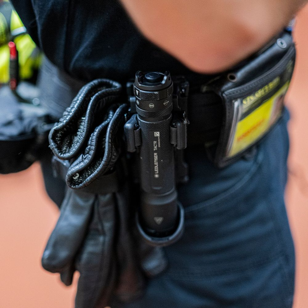 Un policier porte une ceinture utilitaire noire avec des gants et une lampe de poche.
