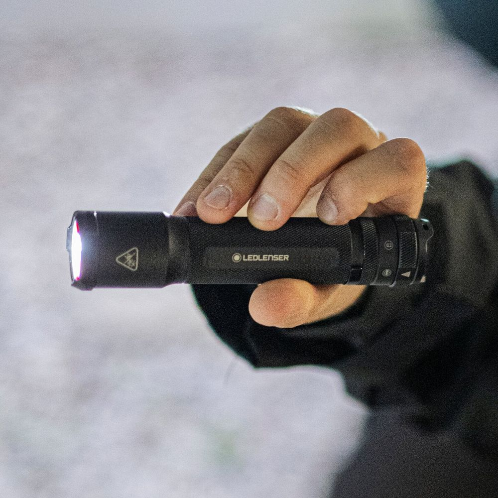 Une main tient une lampe torche Ledlenser noire, allumée à l'avant.