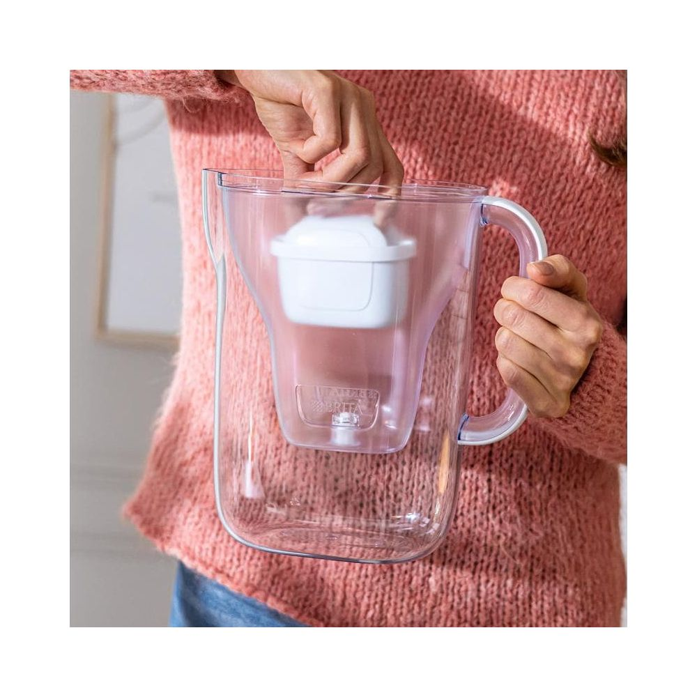 Eine Person mit einem Korallenpullover setzt einen Wasserfilter in einen Krug ein.