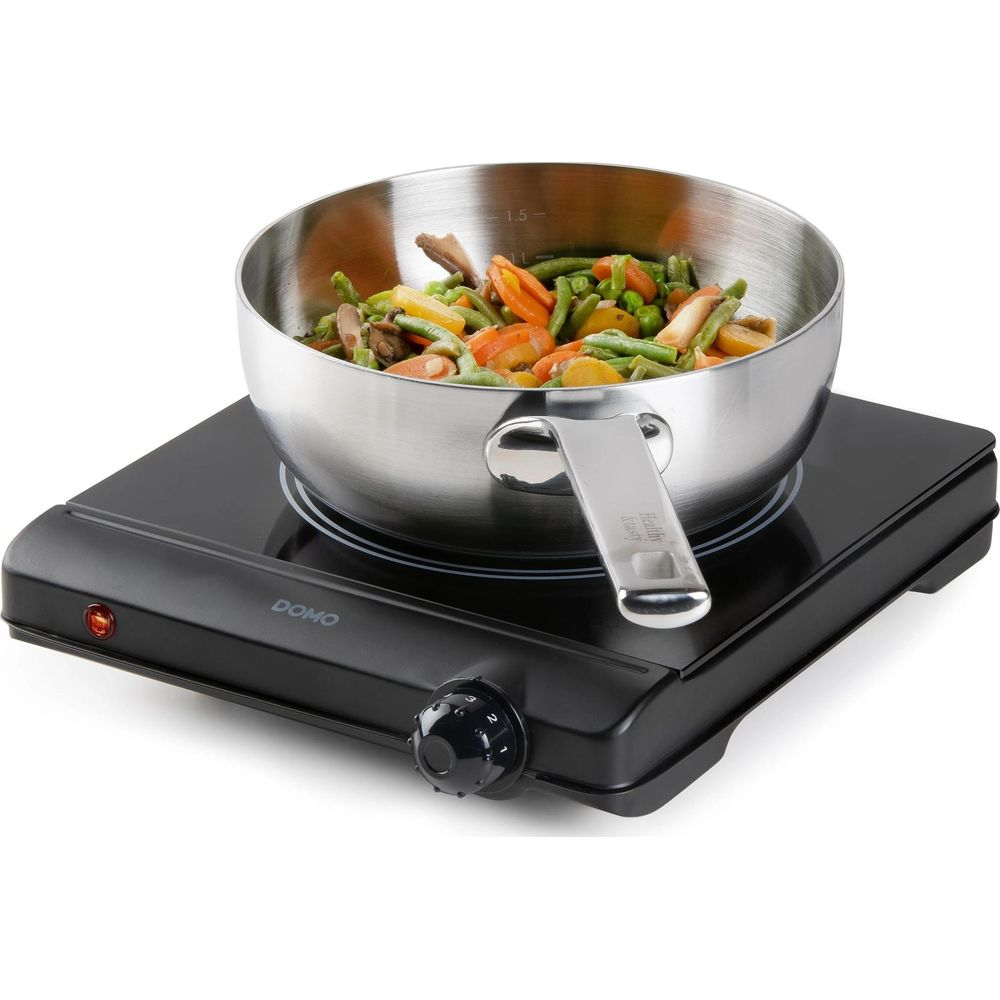Une casserole en acier inoxydable avec des légumes sur une plaque chauffante noire.