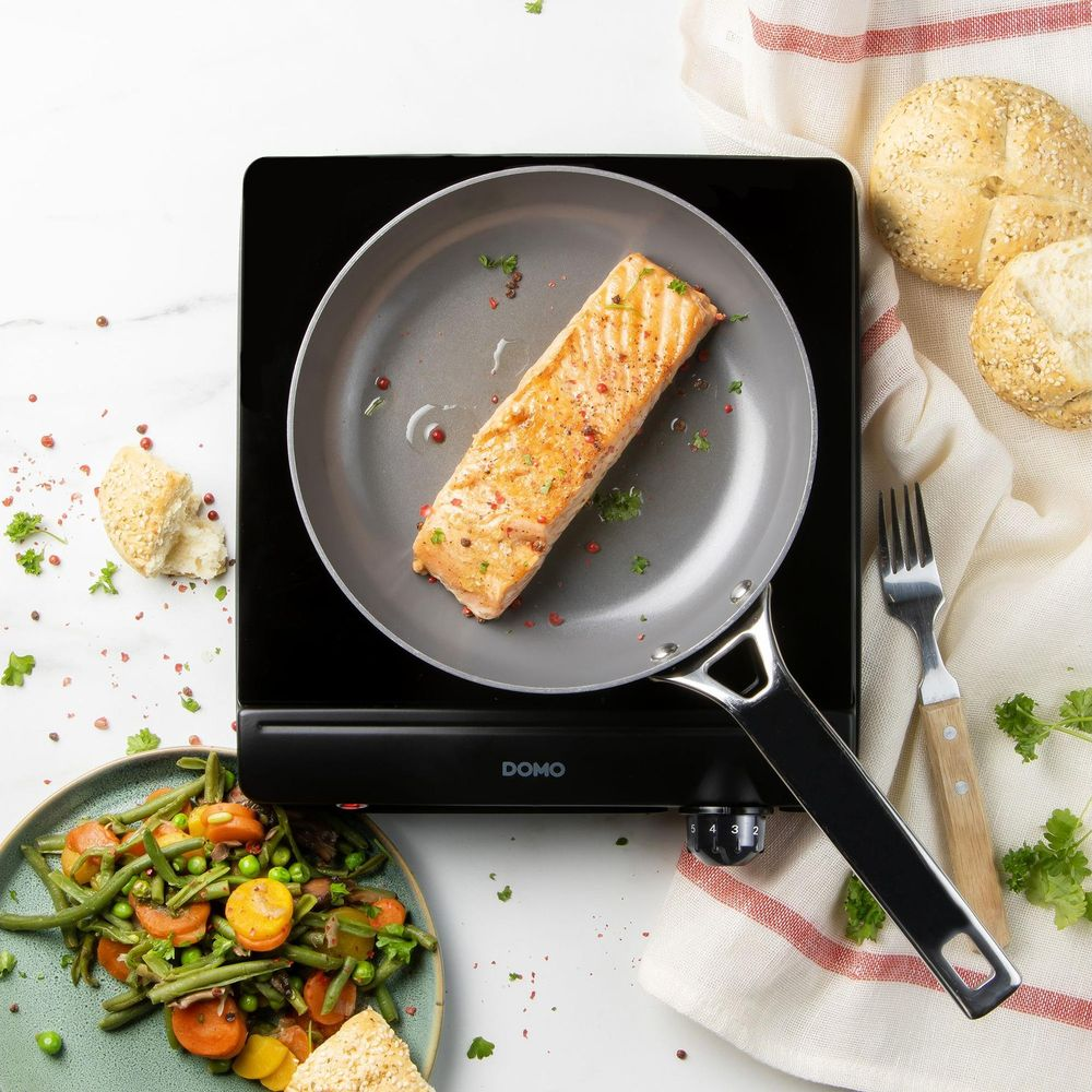 Steak de saumon dans une poêle sur plaque à induction, avec légumes et pains.