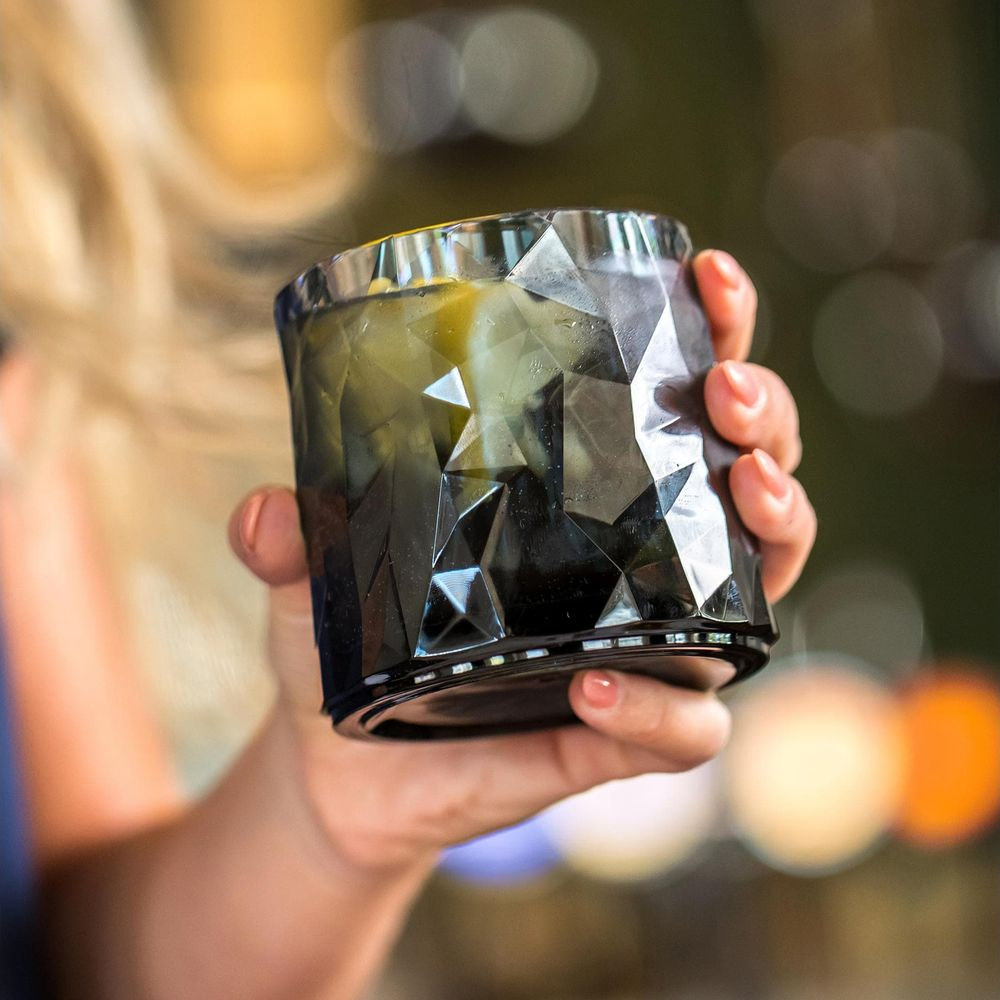 Eine Hand hält ein facettiertes schwarzes Glas mit einem Getränk und Eis.
