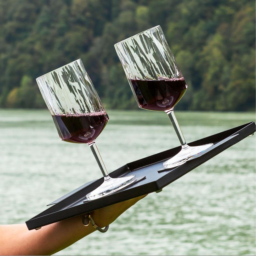 Deux verres de vin rouge sur un plateau noir, paysage extérieur en arrière-plan.