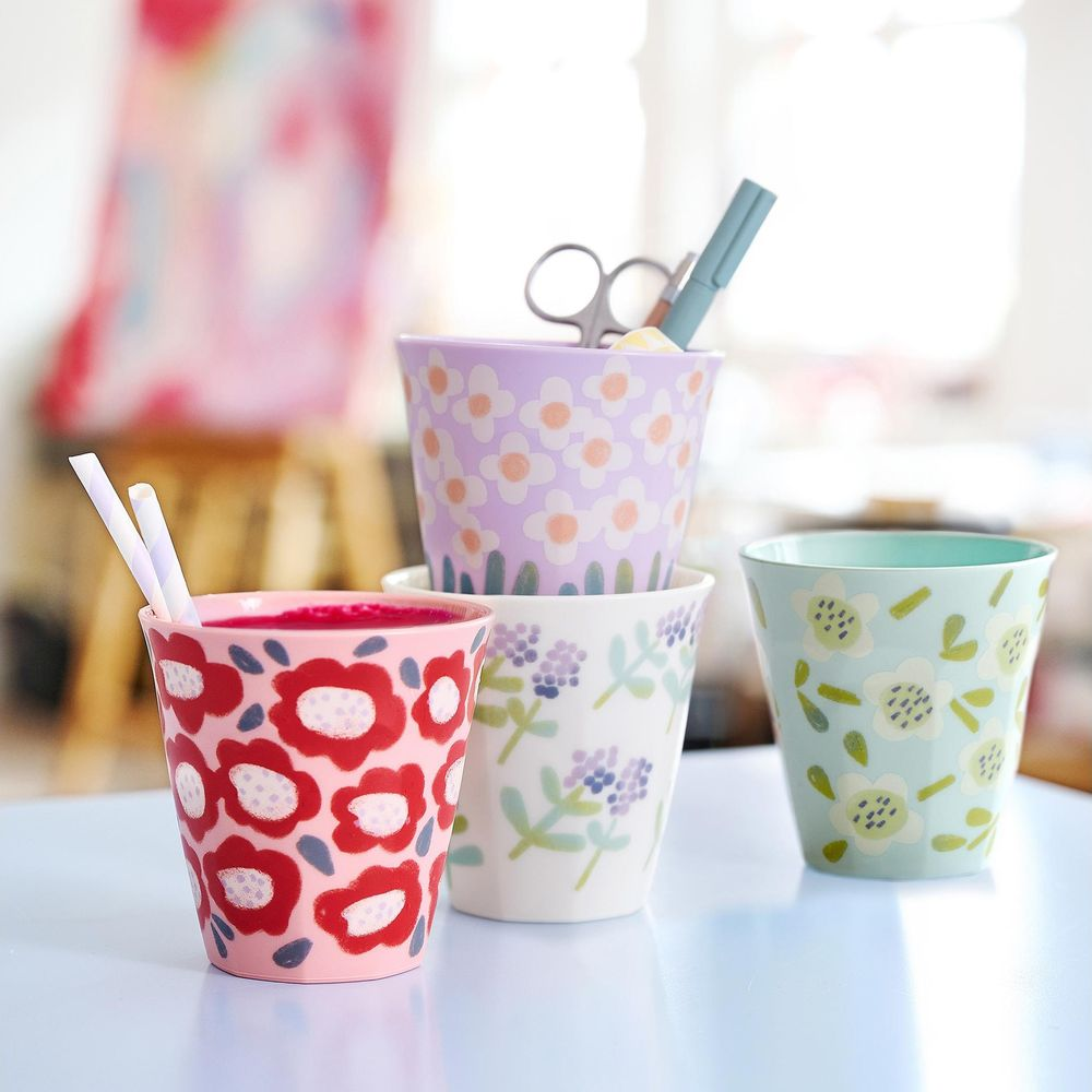 Vier bunte Becher mit Blumenmuster, einer gefüllt mit Getränk und Strohhalmen.