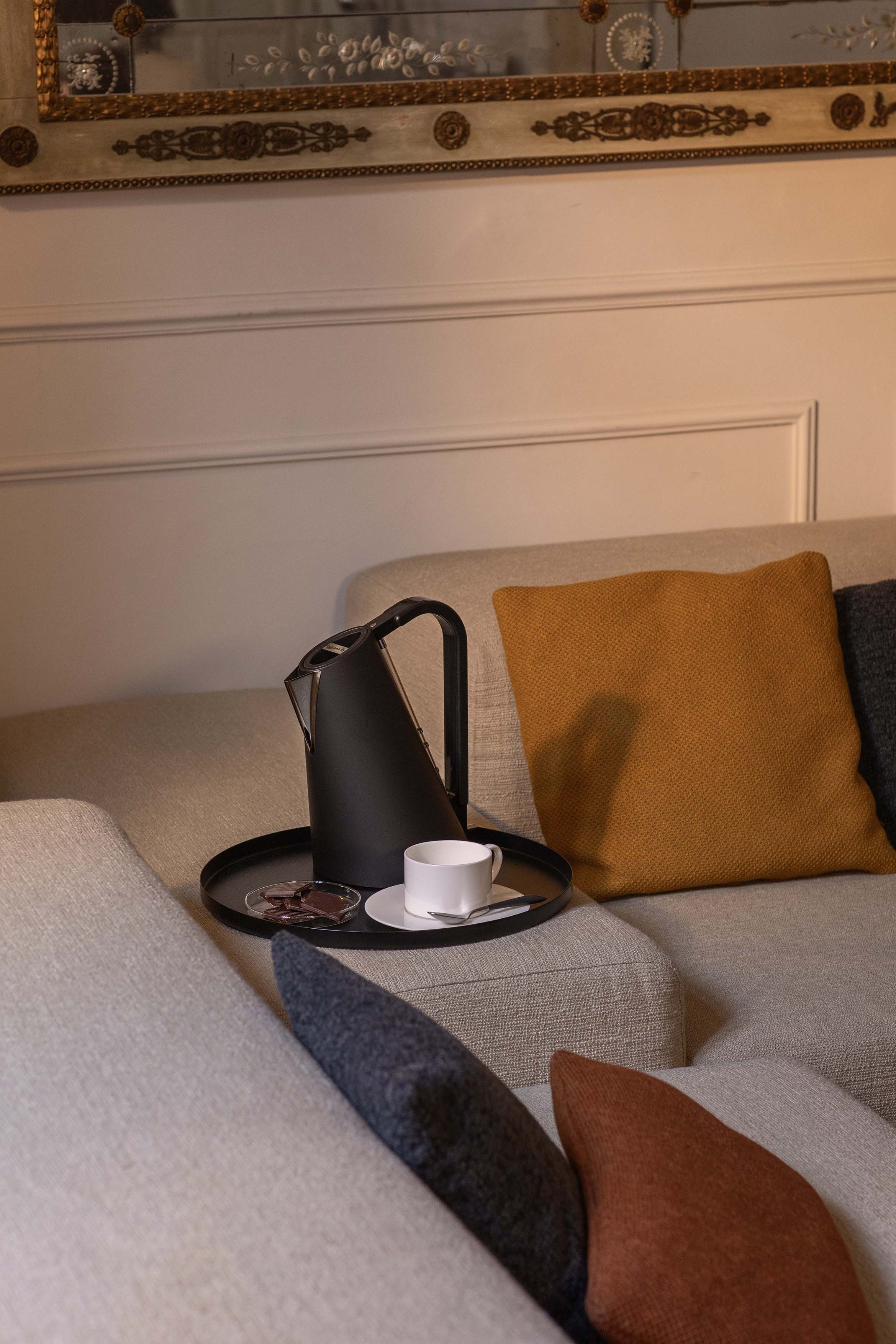 Bollitore nero con tazza e cioccolato su un vassoio sul divano.