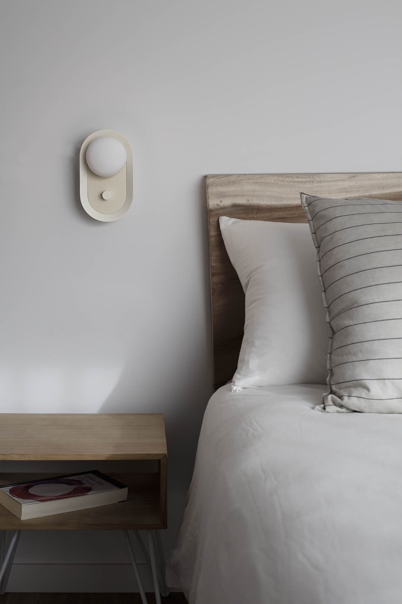 Un comodino in legno con un libro accanto a un letto con lenzuola bianche e cuscini a righe.