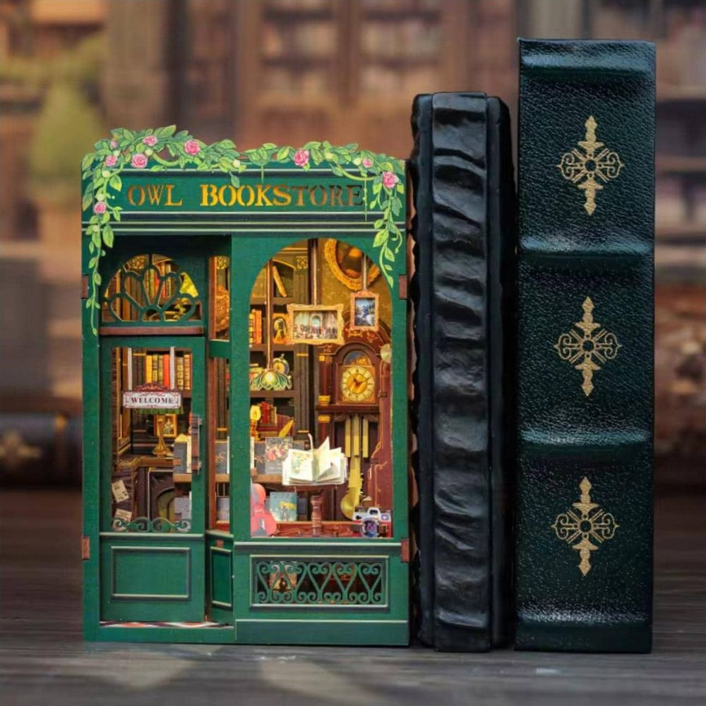 Une librairie miniature verte avec enseigne "Owl Bookstore", intérieur détaillé et deux grands livres.