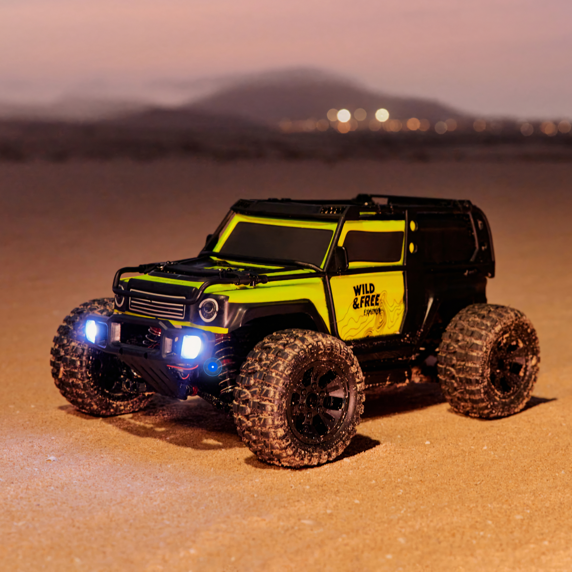 Ein gelber und schwarzer RC-Geländewagen mit eingeschalteten Lichtern auf sandigem Untergrund.