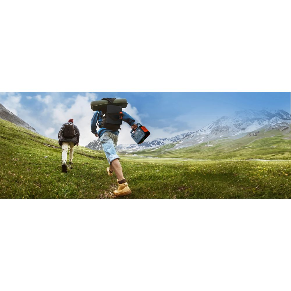 Due escursionisti con zaini corrono su una collina erbosa verso montagne innevate.