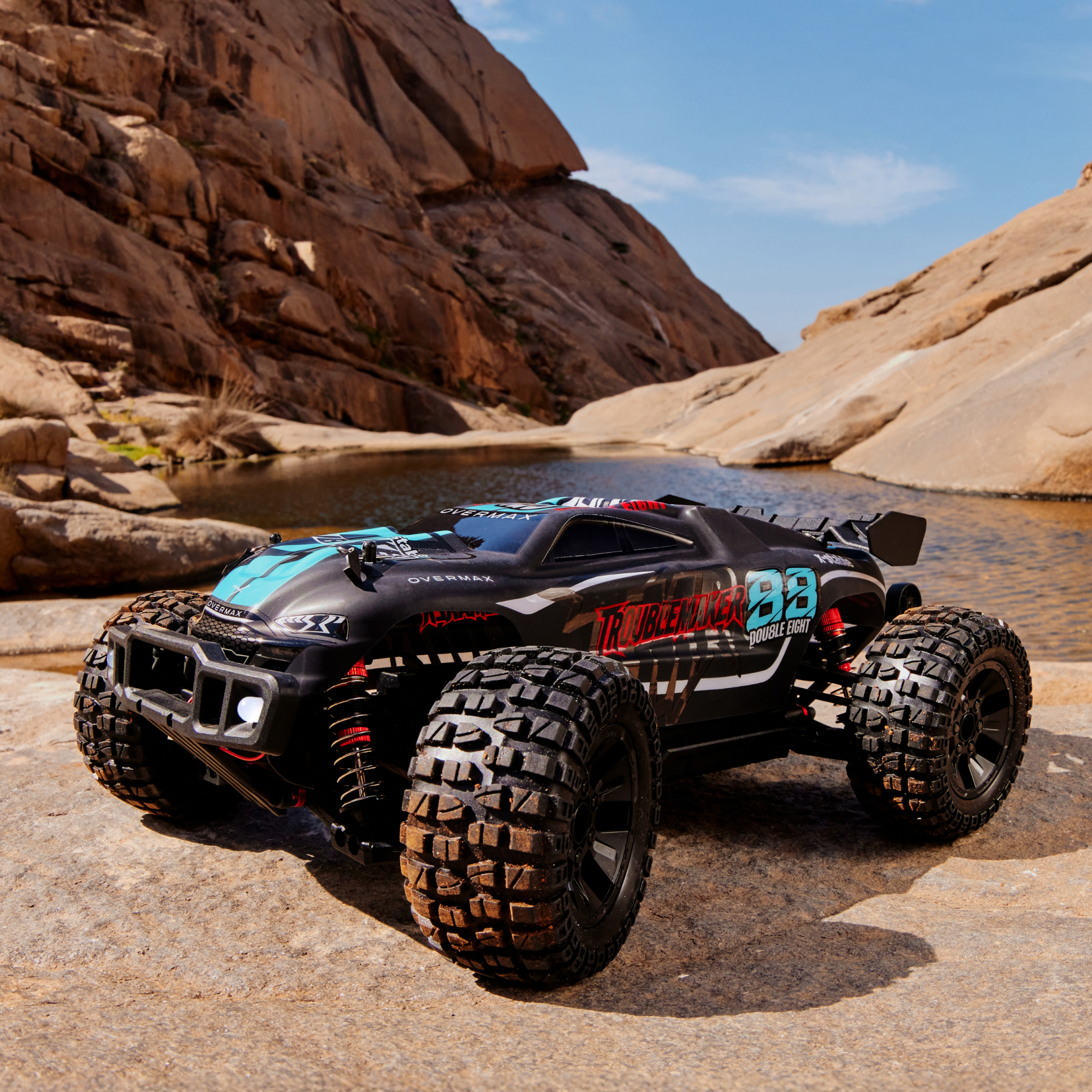 Ein schwarzes RC-Auto mit blauen Akzenten steht auf Felsen neben einem Gewässer.