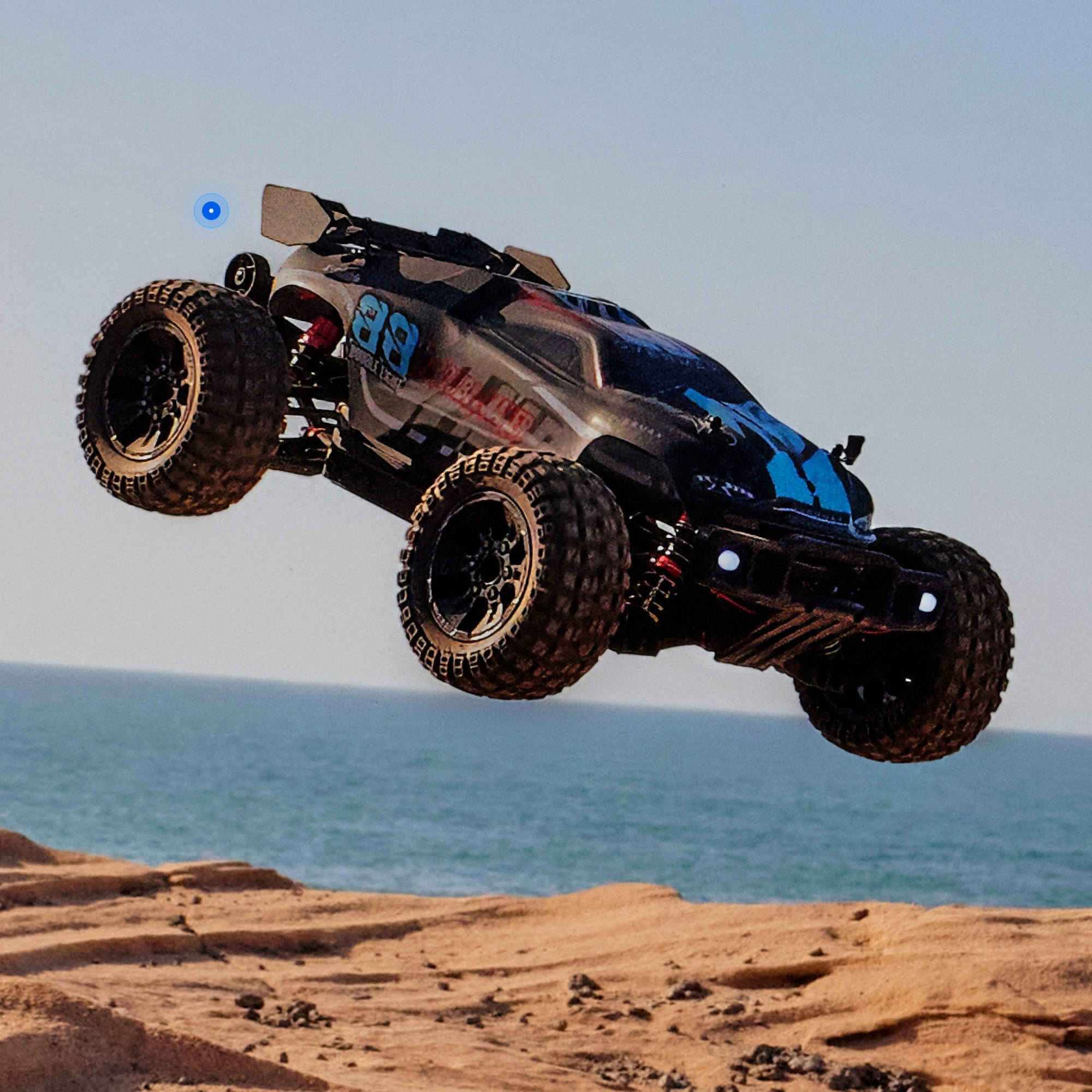 Ein schwarzes ferngesteuertes Auto mit blauen Akzenten springt über eine sandige Klippe am Meer.