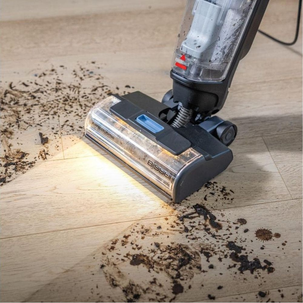 Un aspirateur Bissell avec lumière LED nettoie boue et déversements sur un parquet clair.