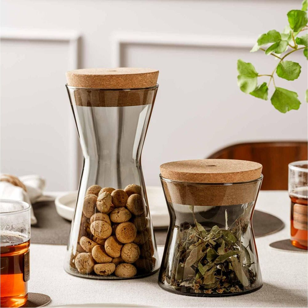 Zwei Glasbehälter mit Korkdeckeln auf einem Tisch, gefüllt mit Keksen und Kräutern.