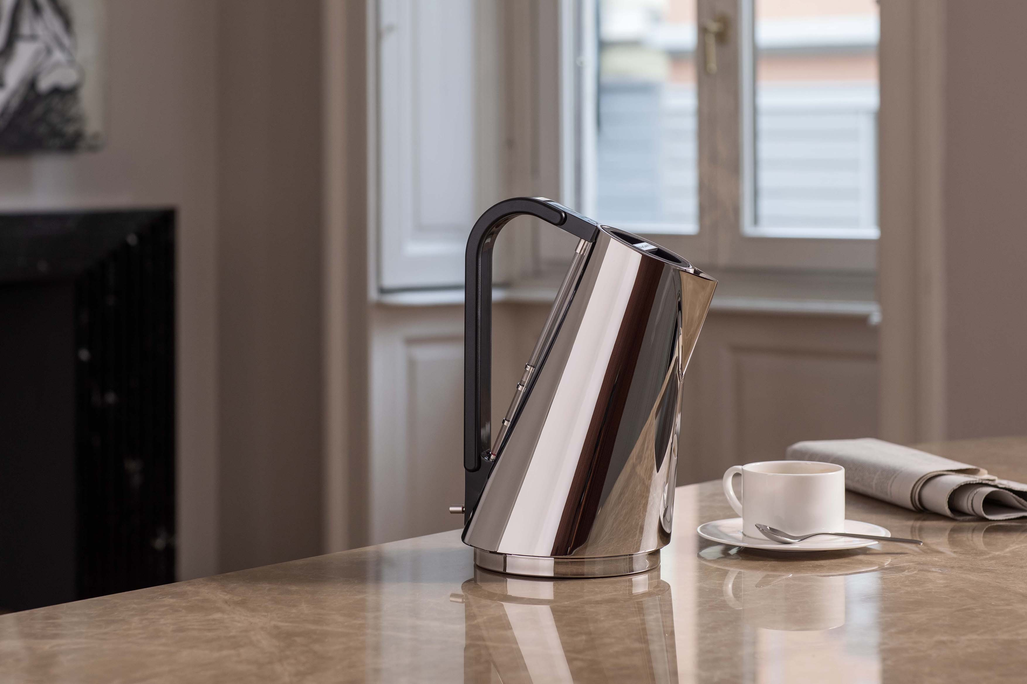 Un bollitore lucido e una tazza di caffè su un tavolo di marmo.