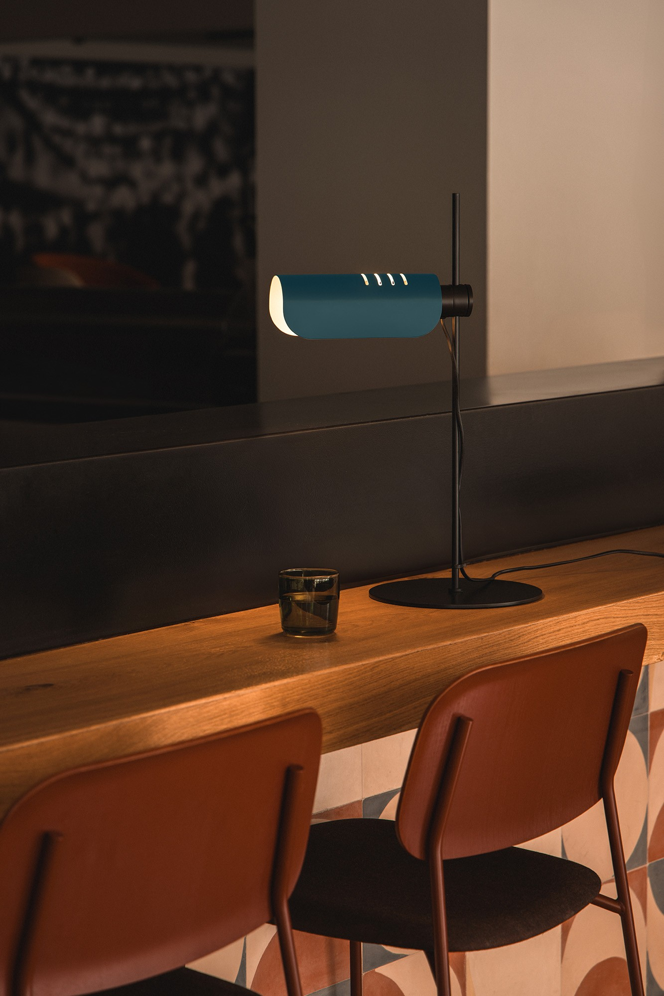 Una lampada da scrivania blu è su un bancone di legno accanto a un bicchiere.