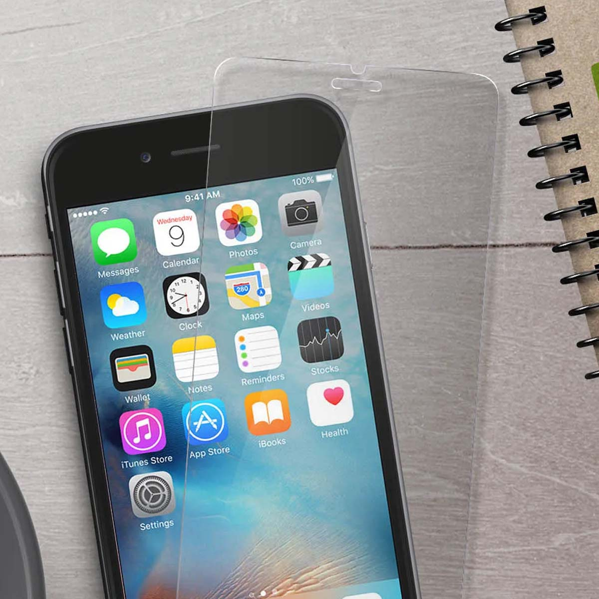 Un iPhone con protezione schermo e un quaderno accanto su sfondo di assi di legno.