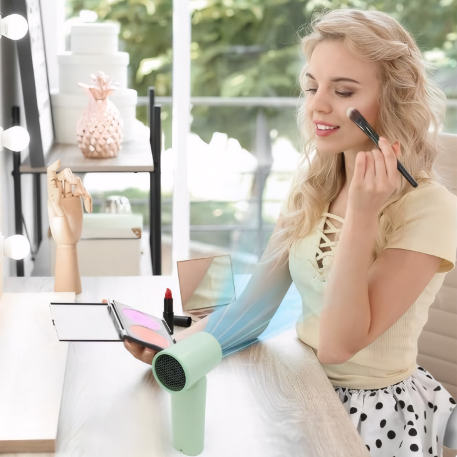 Eine Frau trägt Make-up auf, während ein Minilüfter sie anföhnt.