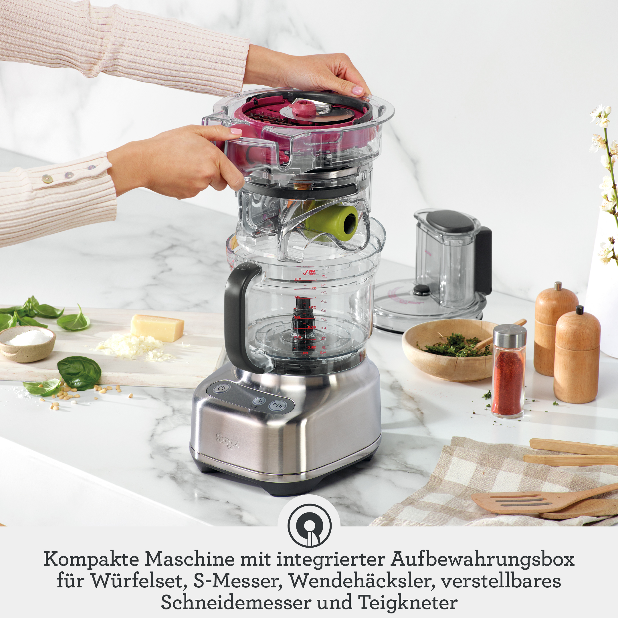 Kompakte Küchenmaschine mit Zubehör wie S-Messer, Würfelset auf Marmorplatte.