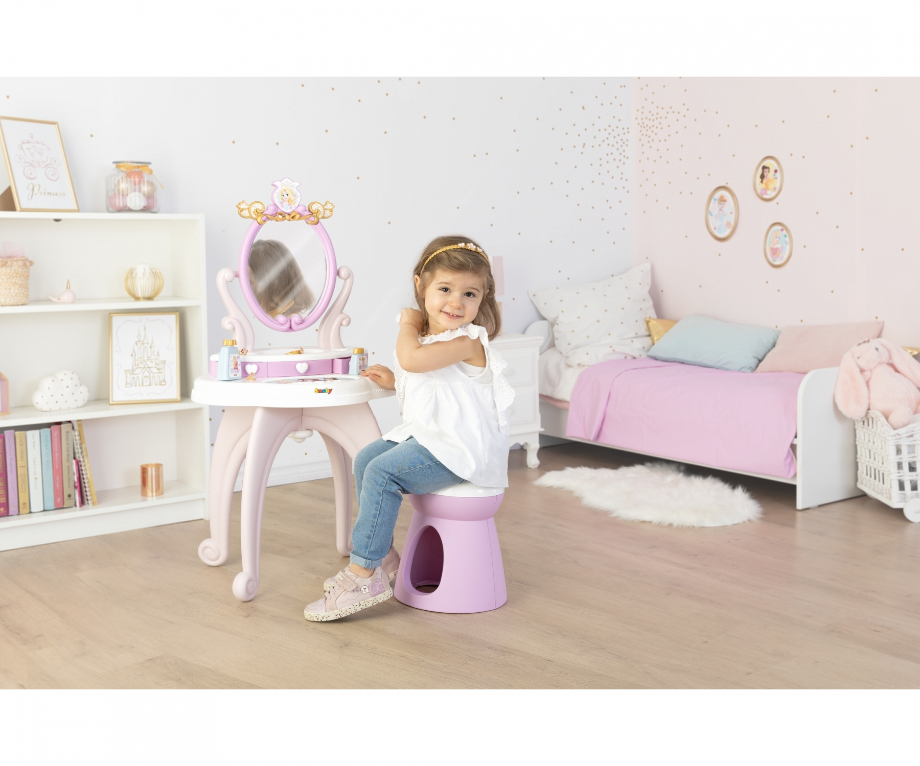 Una bambina siede su uno sgabello viola a un tavolino da toeletta in una camera da letto a tema principessa.
