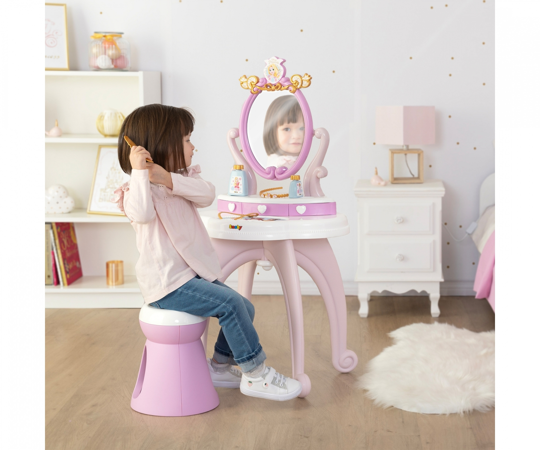 Una bambina si pettina davanti a una toeletta rosa con specchio.