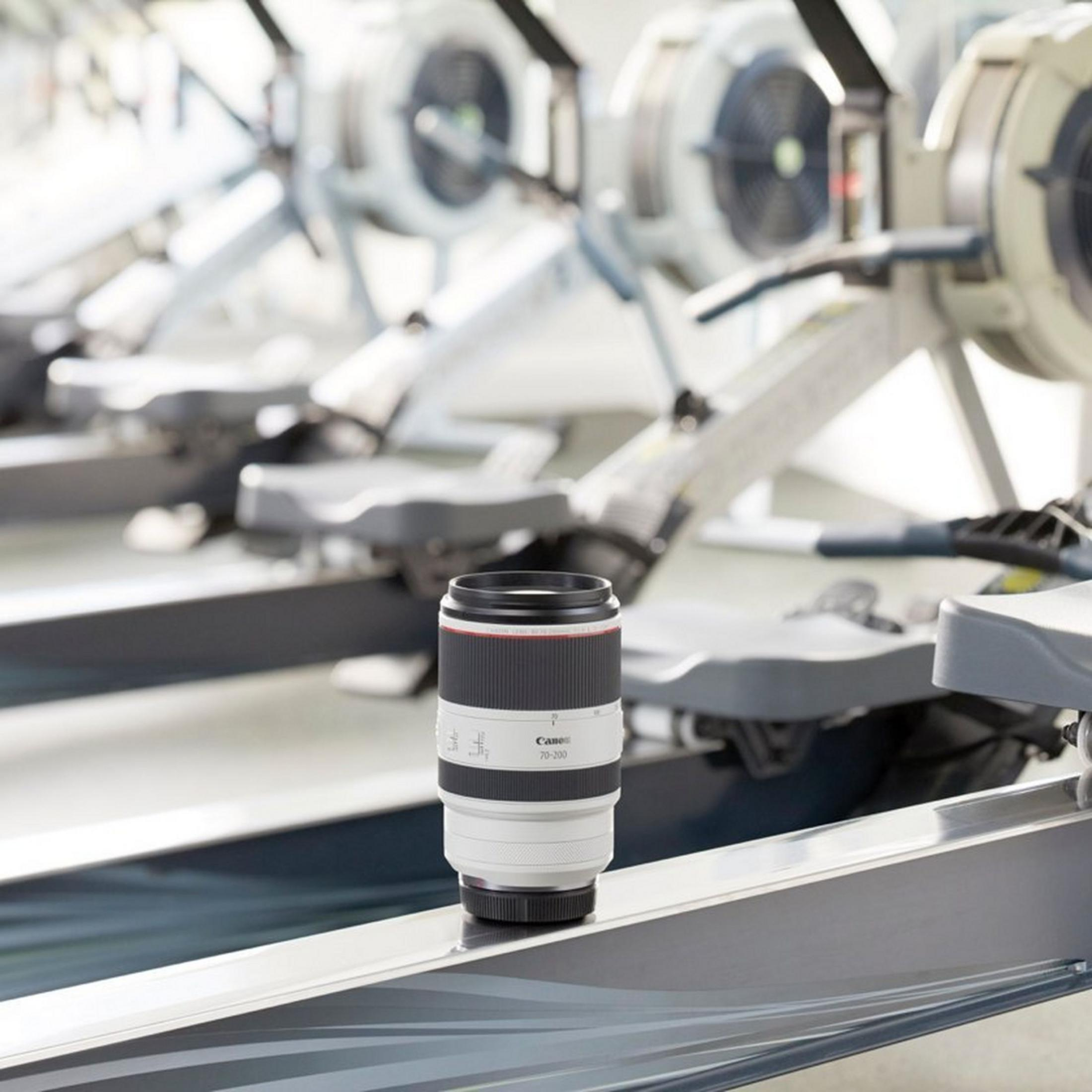 Un obiettivo Canon 70-200mm bianco poggia su una macchina da canottaggio in palestra.