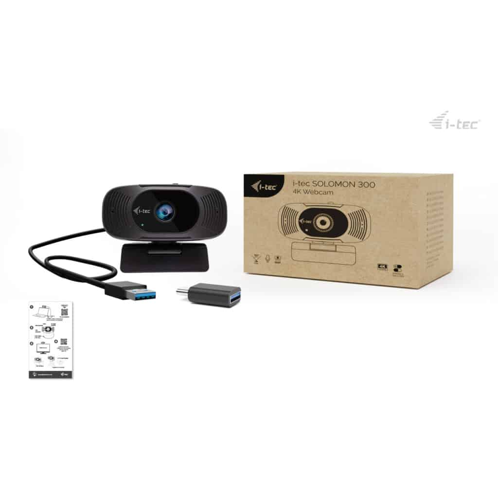 Zwarte webcam met USB-kabel, adapter en productdoos op witte achtergrond.