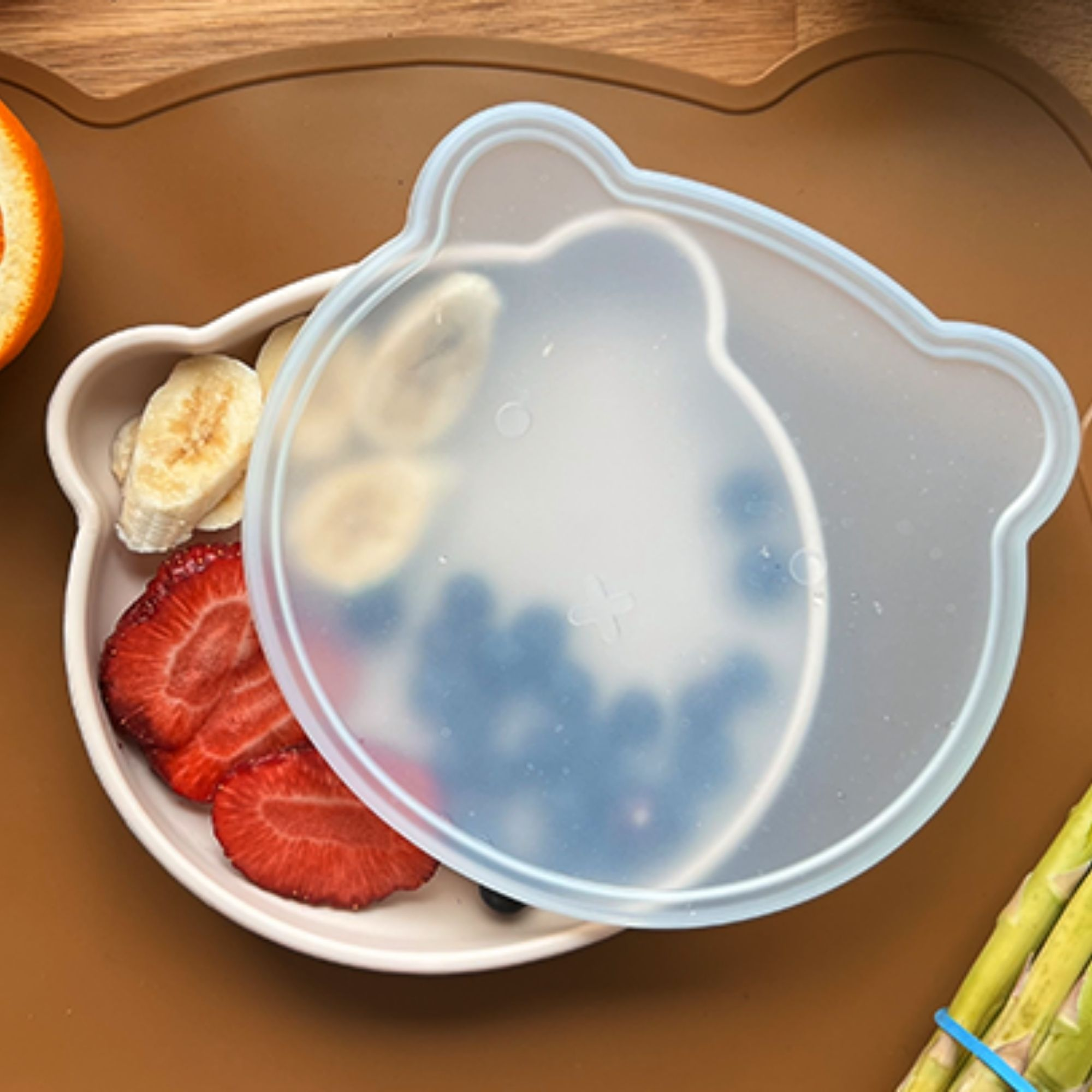 Miseczka w kształcie misia z truskawkami, plasterkami banana i borówkami pod pokrywką.