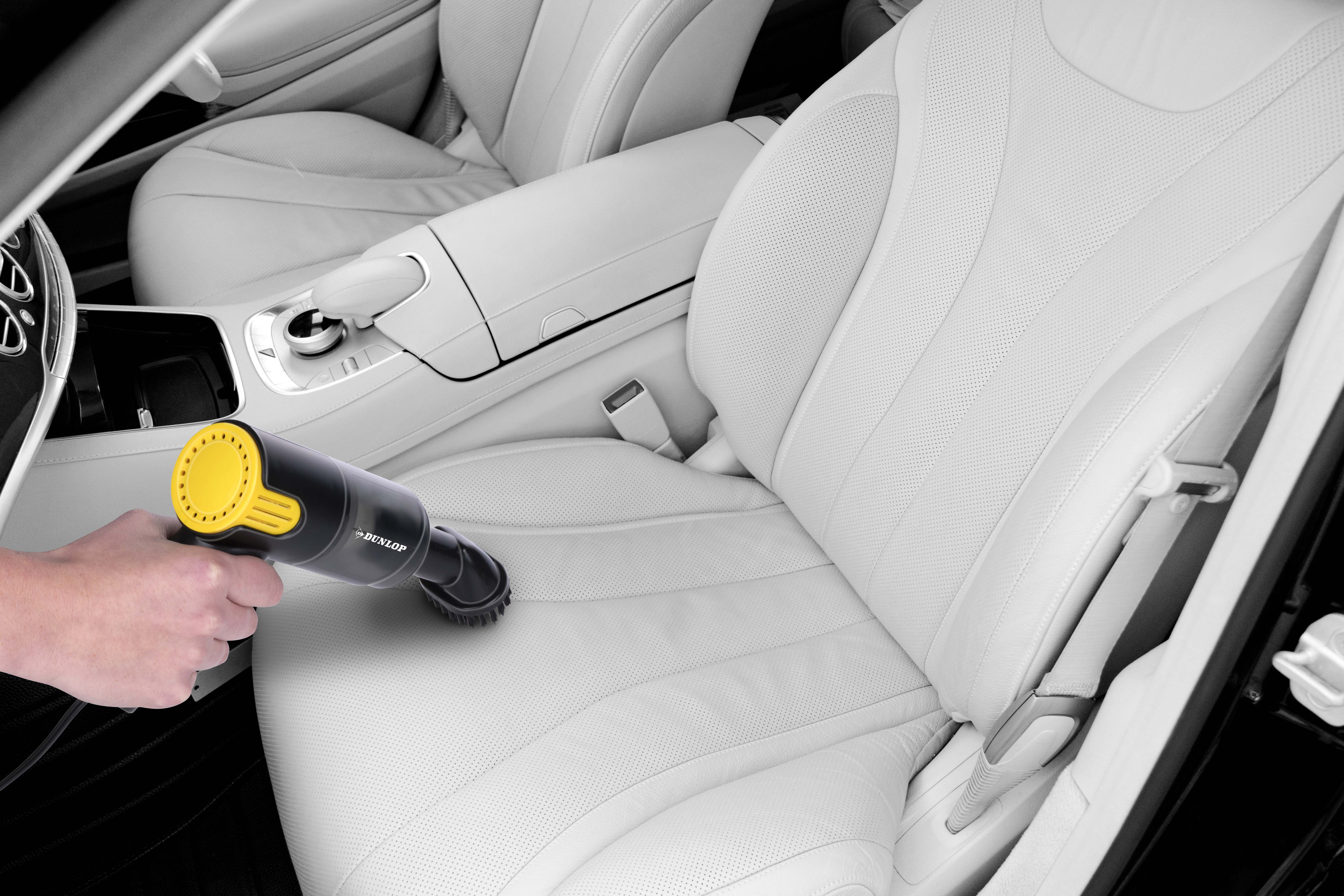Hand vacuums a car interior with white leather seats. Black vacuum with yellow nozzle.