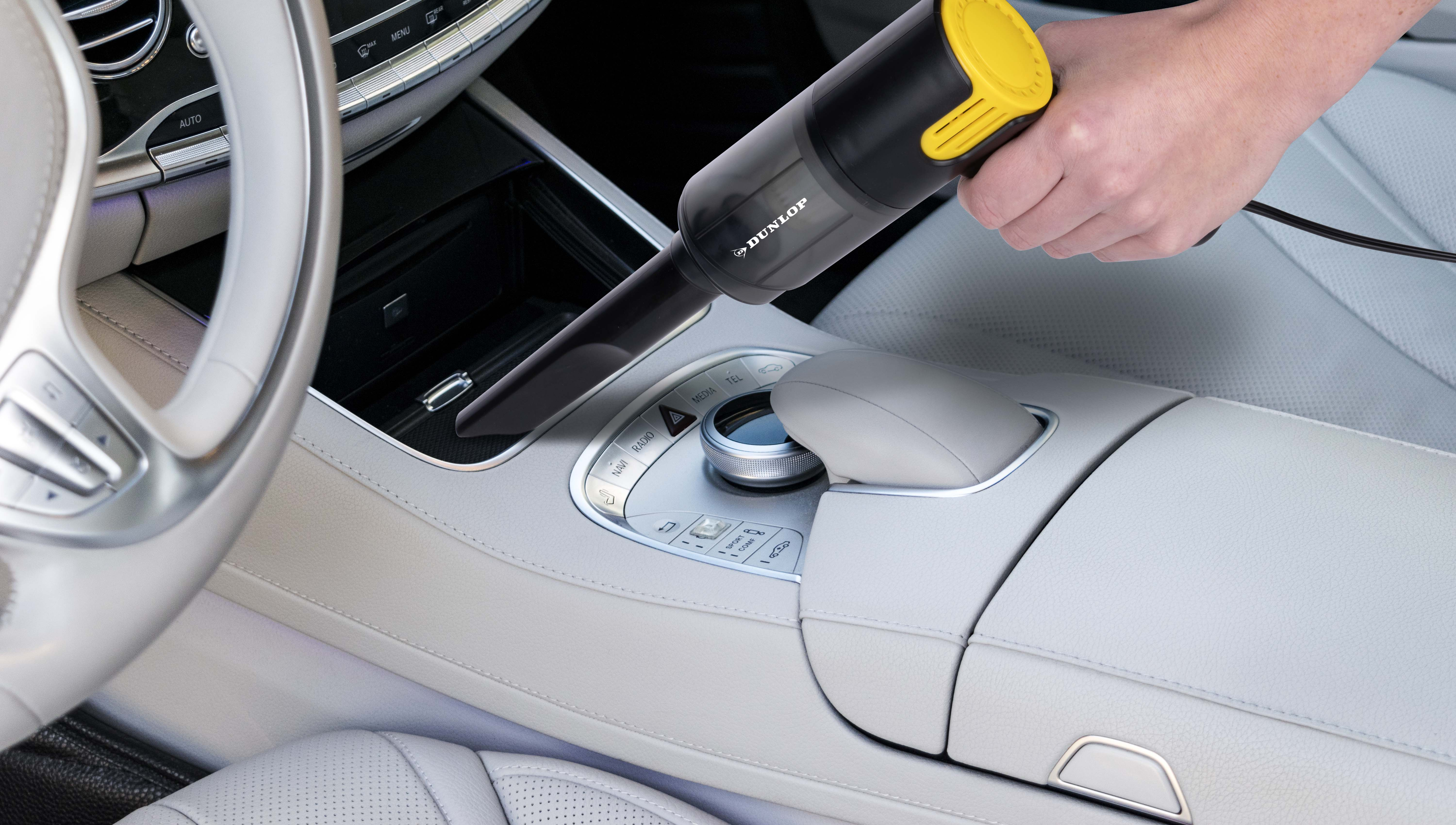 A hand uses a black and yellow handheld vacuum cleaner inside a car.