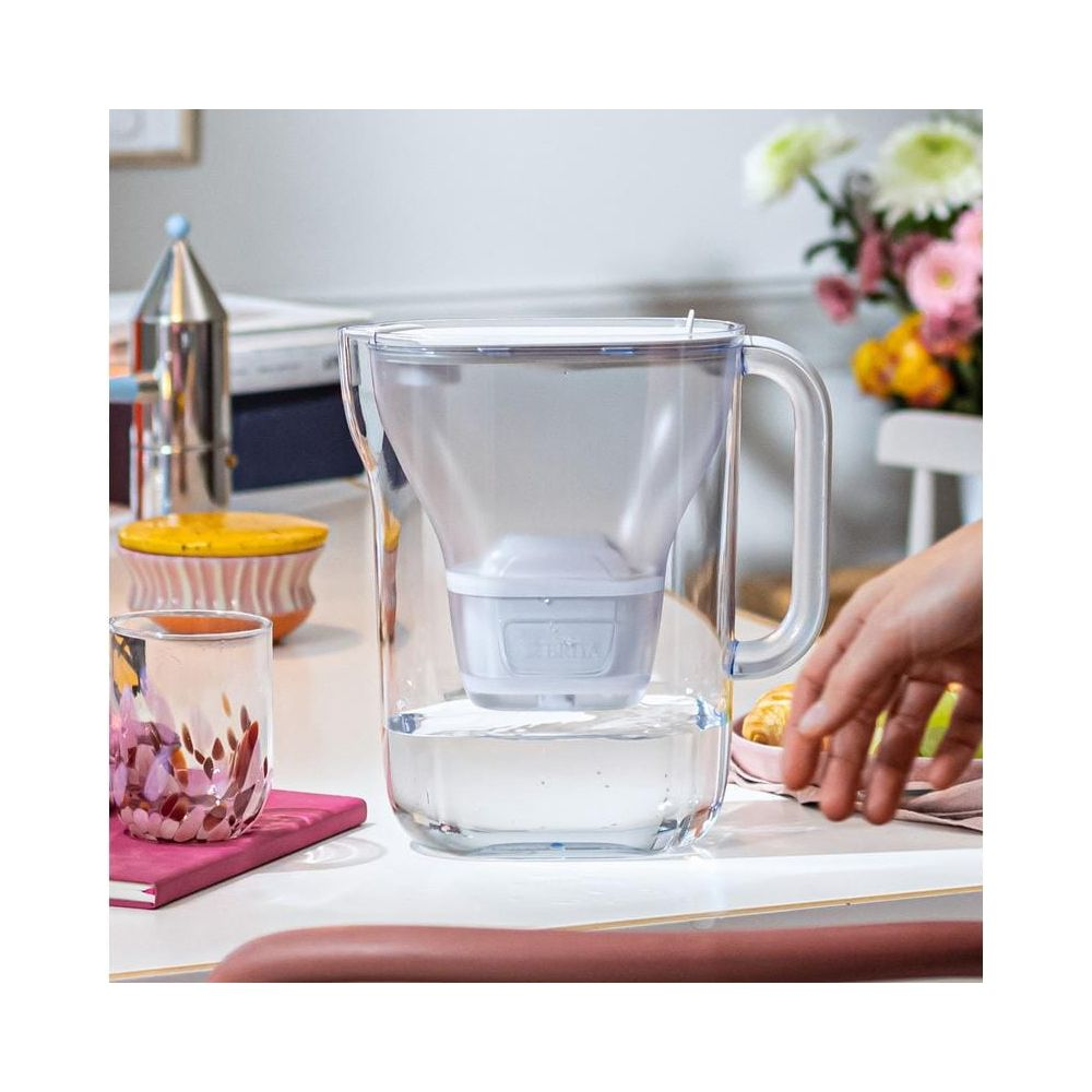 Ein klarer Wasserfilterkrug mit einem Filter und Wasser, auf einem Tisch mit Glas.
