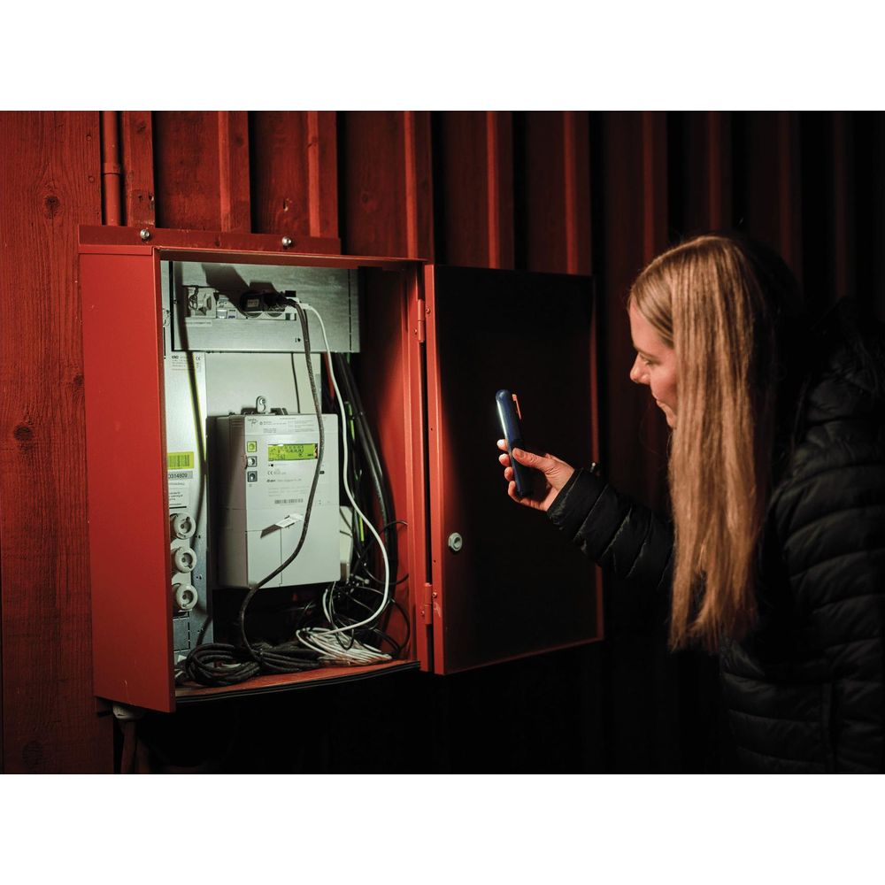 Une femme avec un smartphone éclaire une armoire rouge ouverte avec des compteurs.