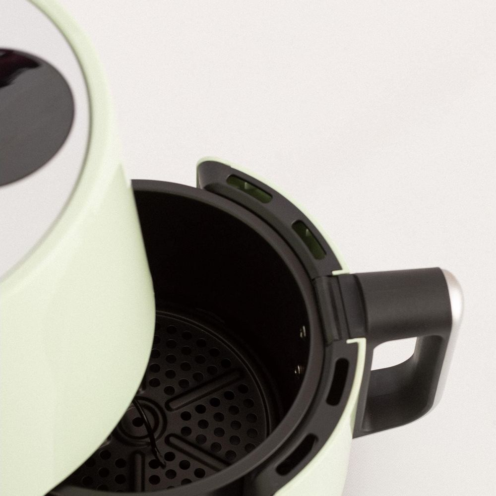Una freidora de aire verde claro con la cesta abierta, mostrando inserto y asa negros.