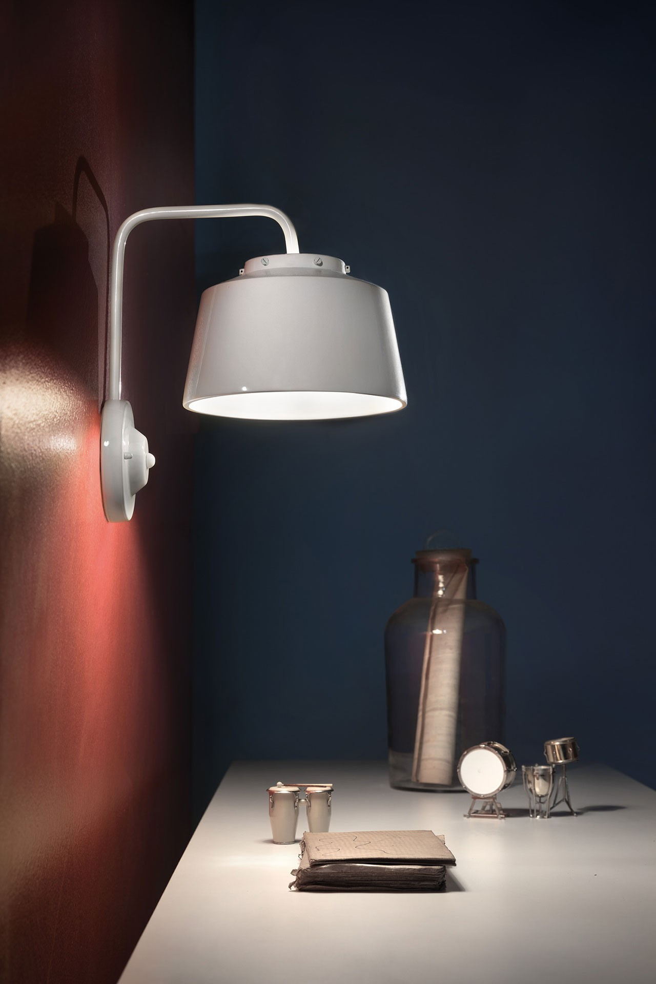 Una lampada da parete bianca illumina una scrivania con oggetti decorativi come tamburi.
