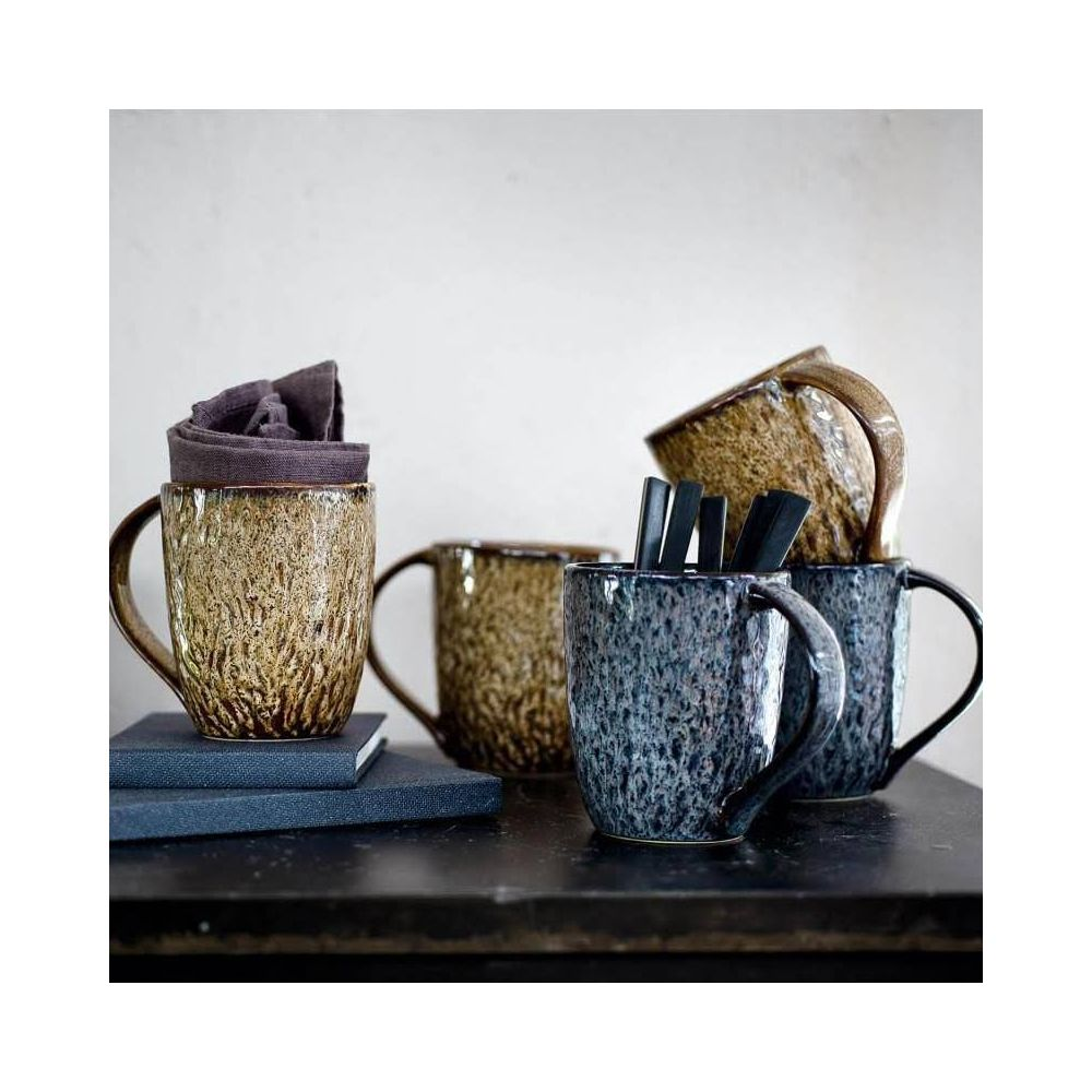 Vier Keramiktassen, braun und blau, stehen auf einem Tisch. Eine Tasse ist mit einem Stoff gefüllt.