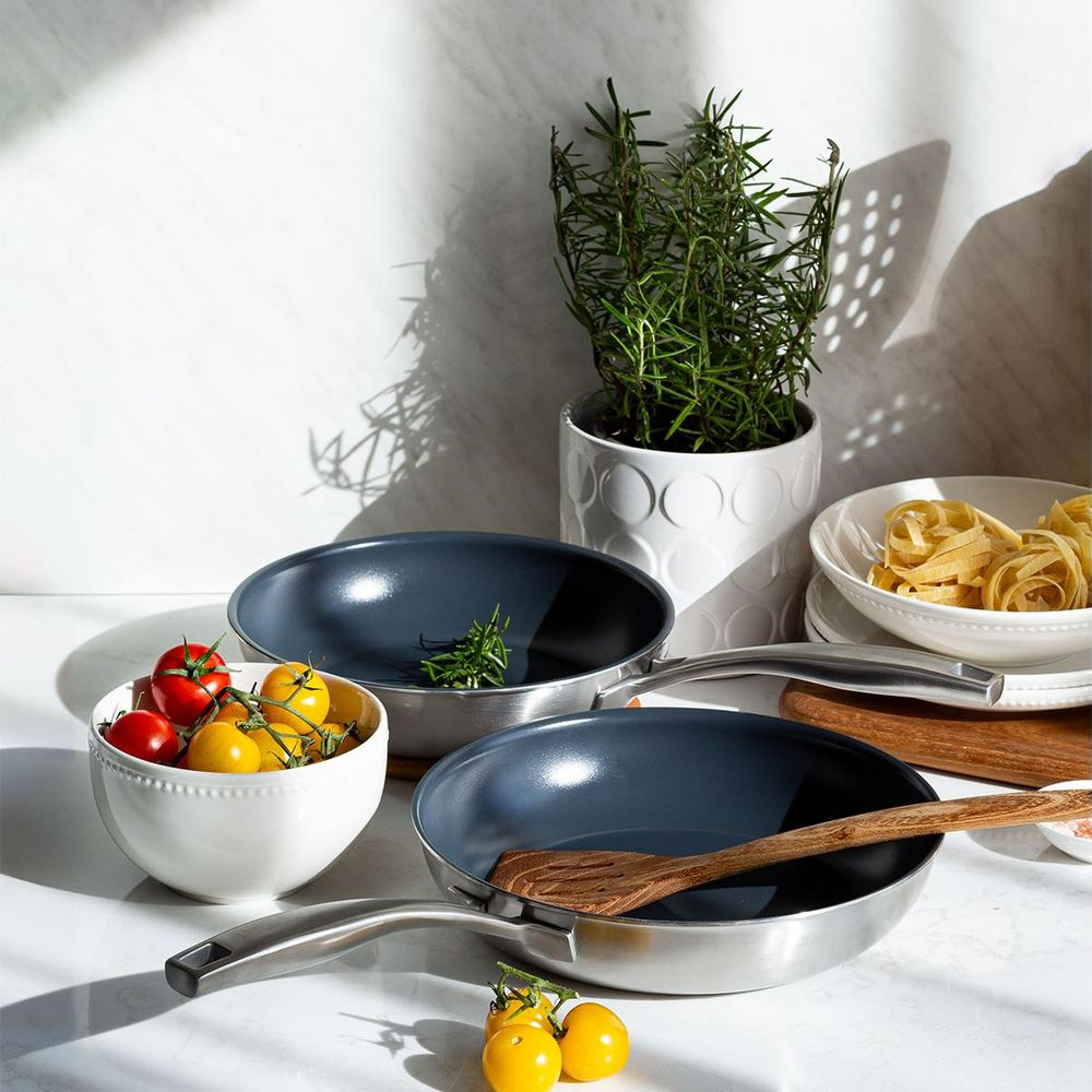 Deux poêles, un bol de tomates, du romarin en pot et des pâtes.