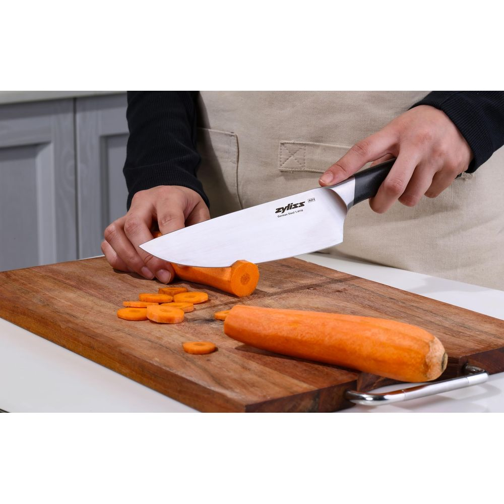 Une personne tranche des carottes sur une planche à découper en bois.