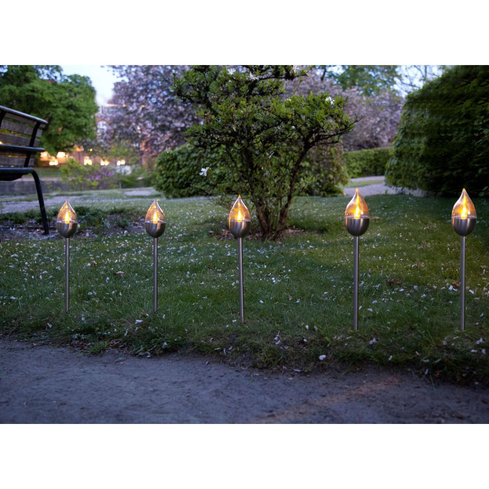 Fünf flammende Gartenleuchten stehen in einer Reihe auf einer Grasfläche.
