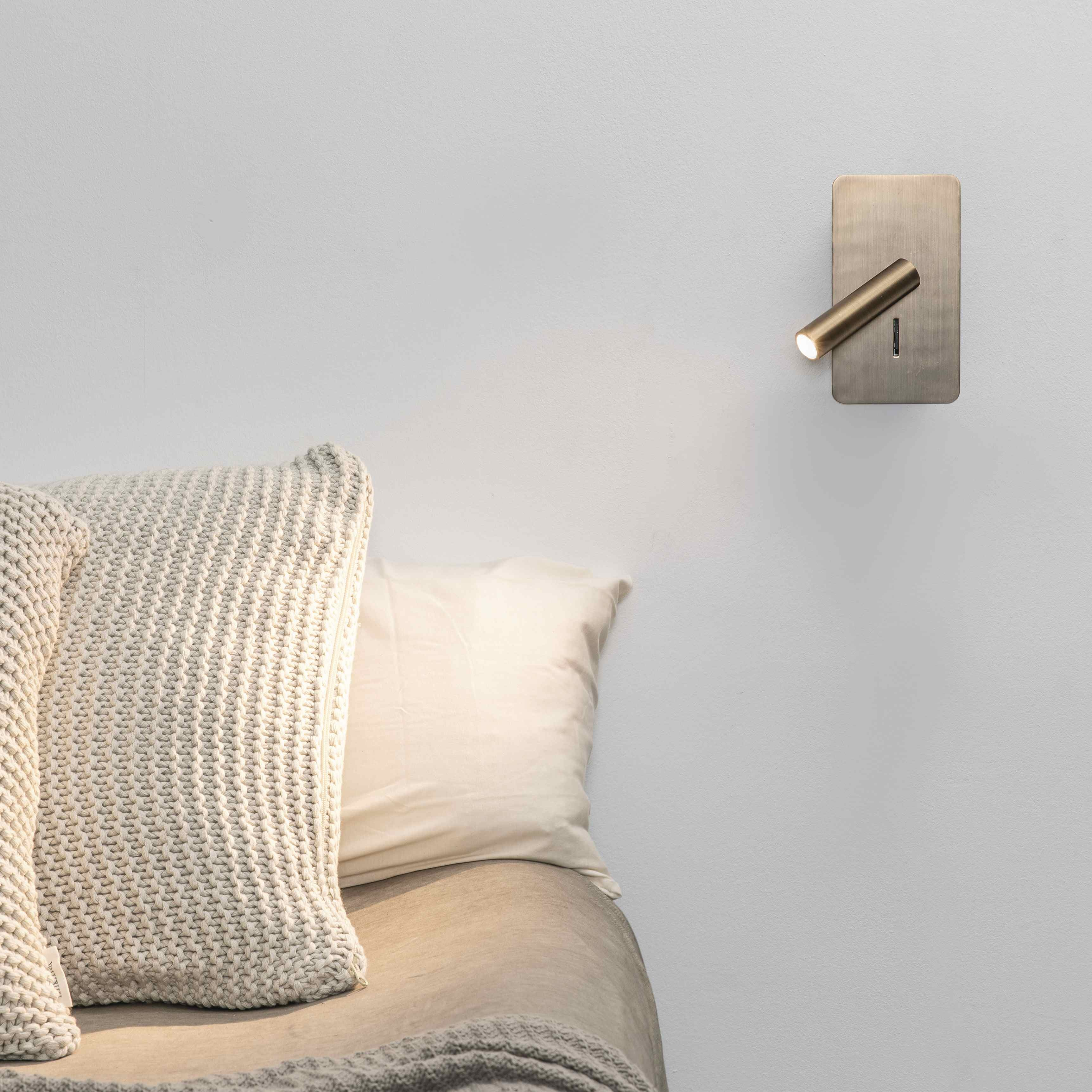 Una lampada da parete moderna illumina due cuscini su un letto.