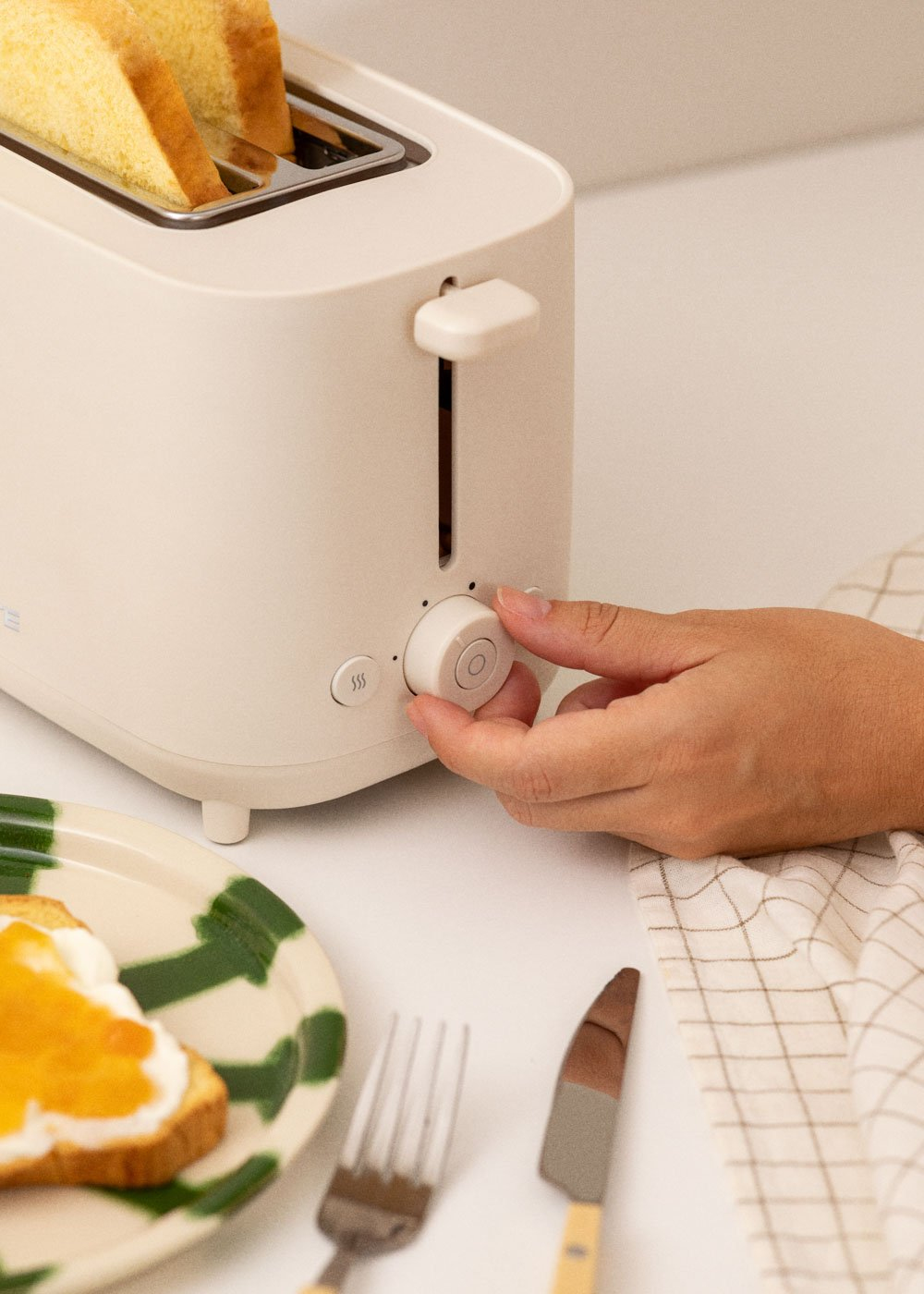 Une main tourne le bouton d'une grille-pain blanche avec du pain.