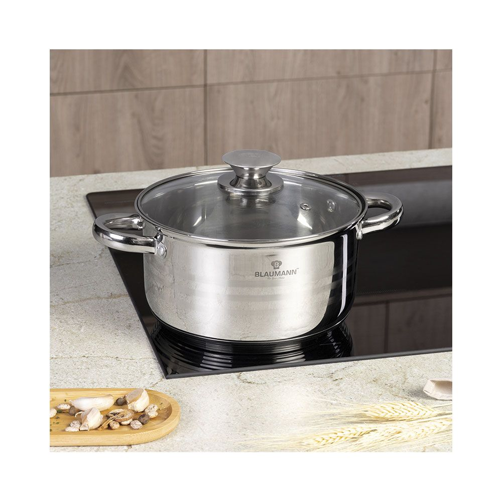 Une cocotte en inox avec couvercle en verre sur plaque à induction noire. Ail et haricots sur plat en bois.