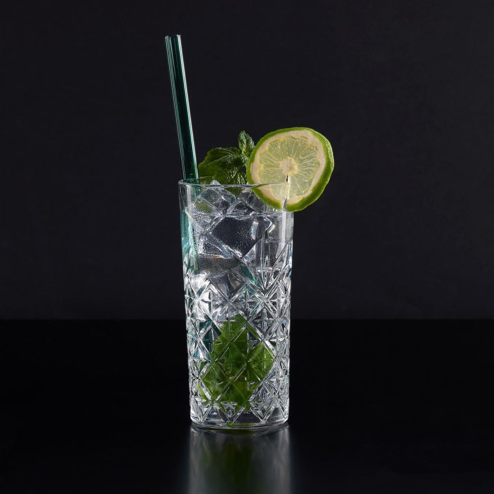 Ein Glas mit einem Getränk, Eiswürfeln, Limettenscheibe, Minze und Strohhalm.