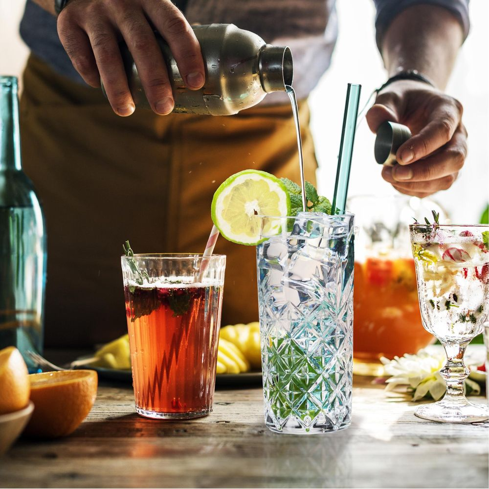 Barkeeper gießt klare Flüssigkeit aus Shaker in ein Glas mit Eis und Minze.