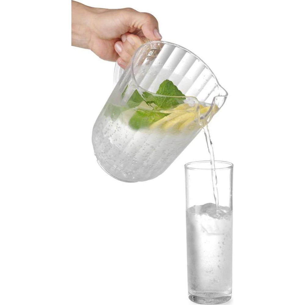 Una mano versa acqua infusa con menta e limone da una brocca in un bicchiere.