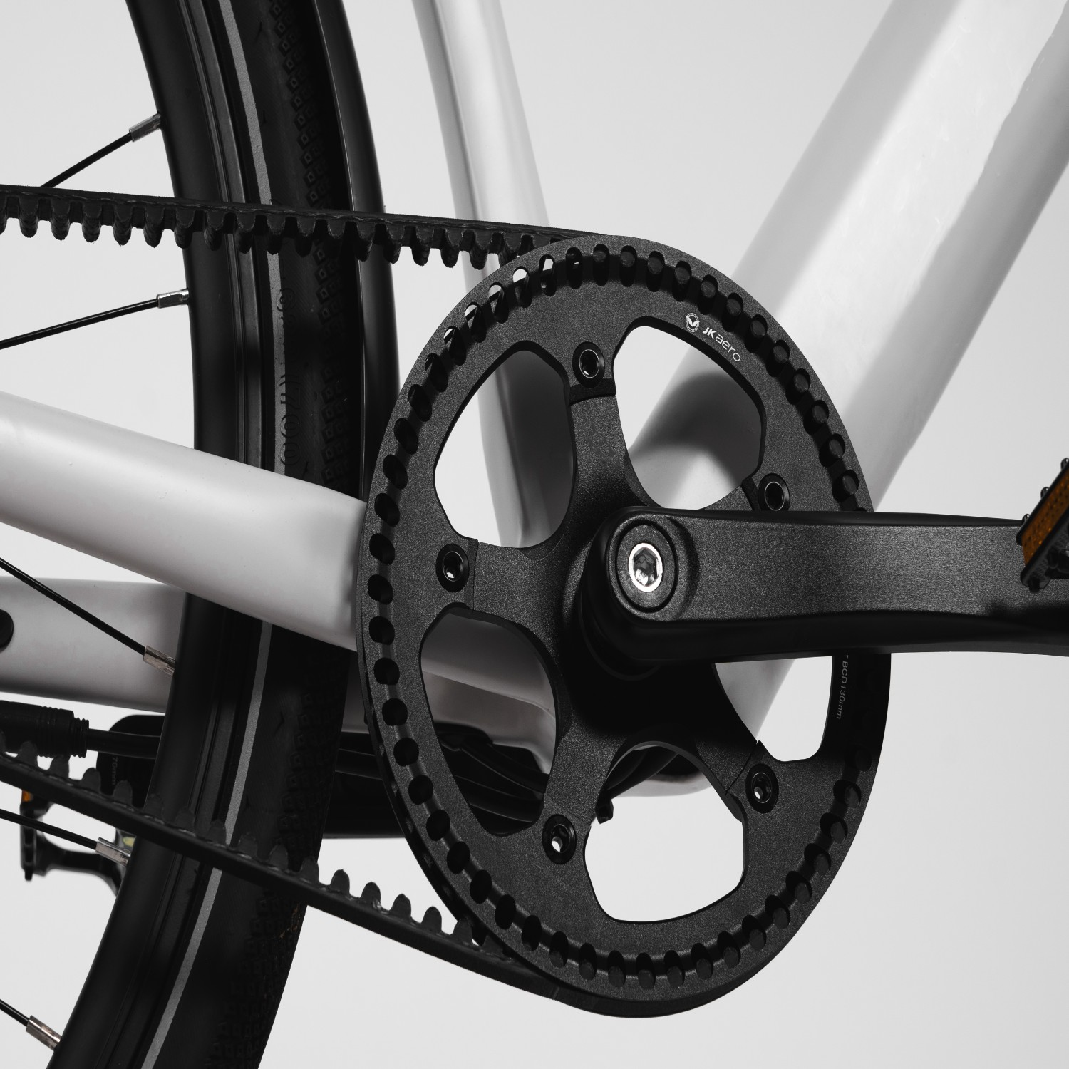 Primer plano de la transmisión por correa y plato de bicicleta negros sobre un cuadro blanco.