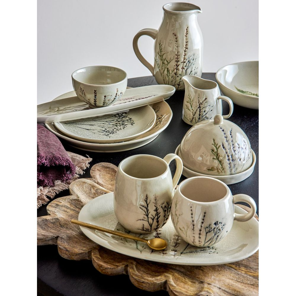 Assiettes et tasses en céramique claire motif lavande sur table sombre.