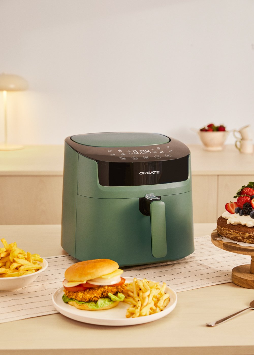 Friggitrice ad aria verde con hamburger, patatine e torta. Scena tavolo cucina.