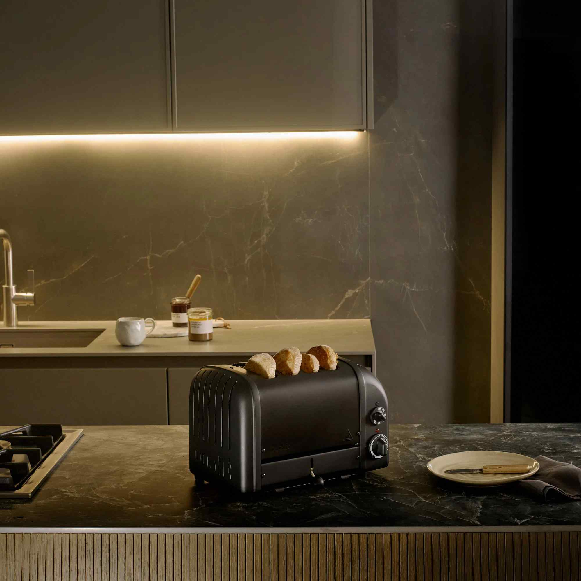Schwarzer Toaster mit Toastbrot, daneben ein Teller mit Messer und eine Tasse.