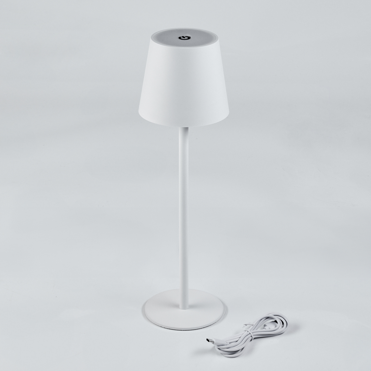 Eine weiße Tischlampe mit einem kegelförmigen Schirm und einem runden Sockel. Ein weißes USB-Kabel liegt daneben.