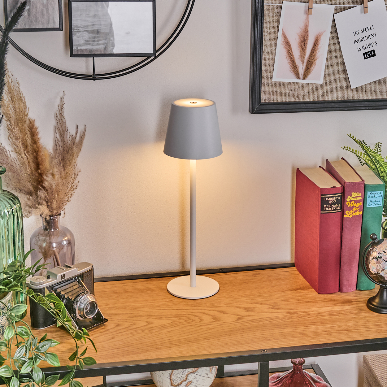 Ein grauer Lampenschirm leuchtet auf einem Schreibtisch mit Büchern.